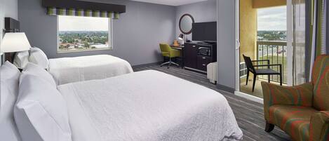 A hotel room with two beds, a desk with a chair, a small round mirror, and a balcony with a chair.