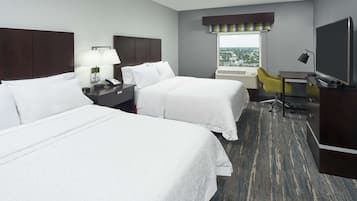 A hotel room with two beds, a desk, a chair, a TV, and a window with a view.