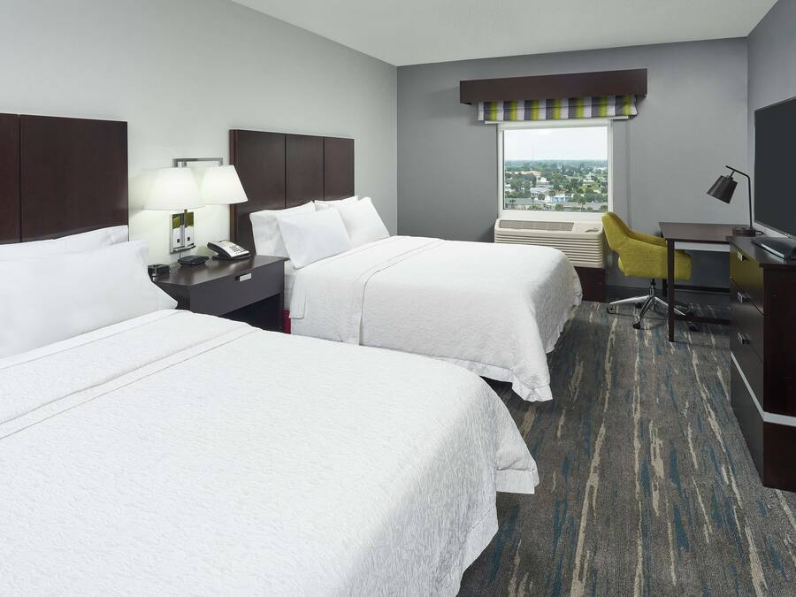 A hotel room with two beds, a desk, a chair, a TV, and a window with a view.