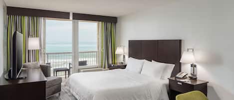 Un cuarto de hotel con cama, escritorio, silla, televisión, teléfono y vista al océano.