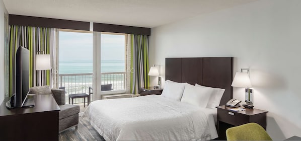 Un cuarto de hotel con cama, escritorio, silla, televisión, teléfono y vista al océano.