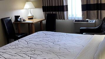 A hotel room with a bed, a desk with a lamp, a chair, a ceiling fan, and a window with curtains.