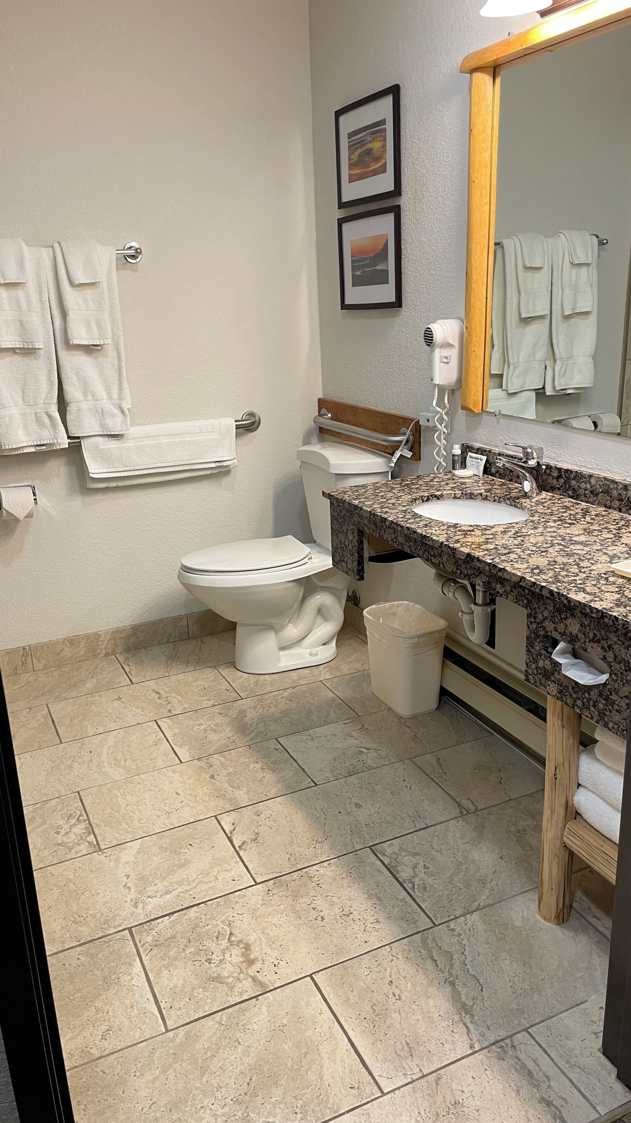 A bathroom with a toilet, sink, and mirror. There are towels hanging on the wall and a trash bin.