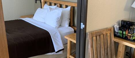 Una habitación de hotel con una cama, una mesita de noche de madera, una silla y un escritorio con lámpara.