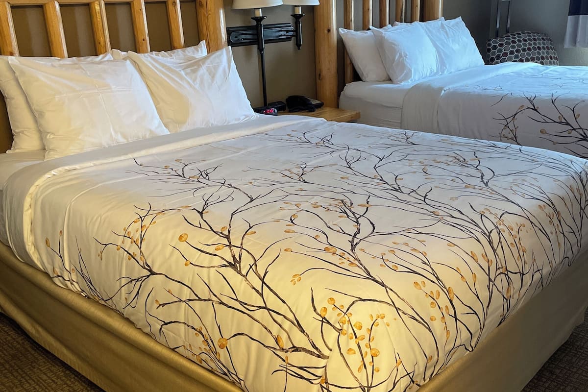 A hotel room with two beds, wooden headboards, white bedding, and a patterned bedspread.