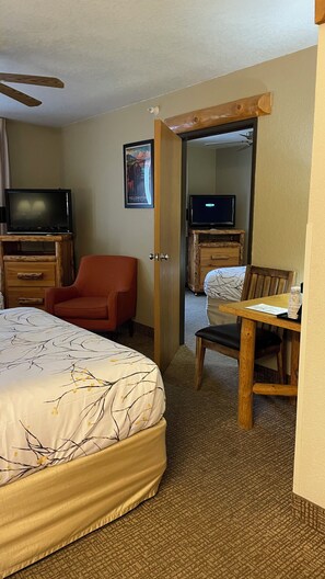 Quarto de hotel com uma cama, escrivaninha, cadeira, televisão e espelho.