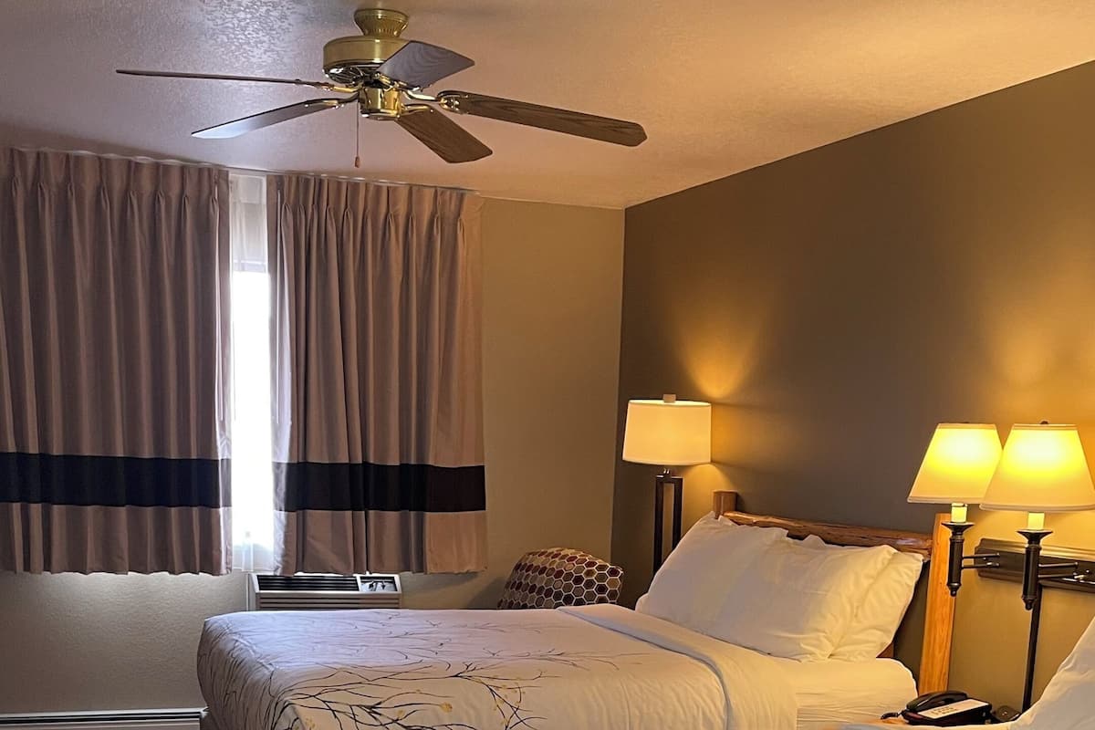 A hotel room with two beds, a ceiling fan, a window with curtains, and two bedside lamps.