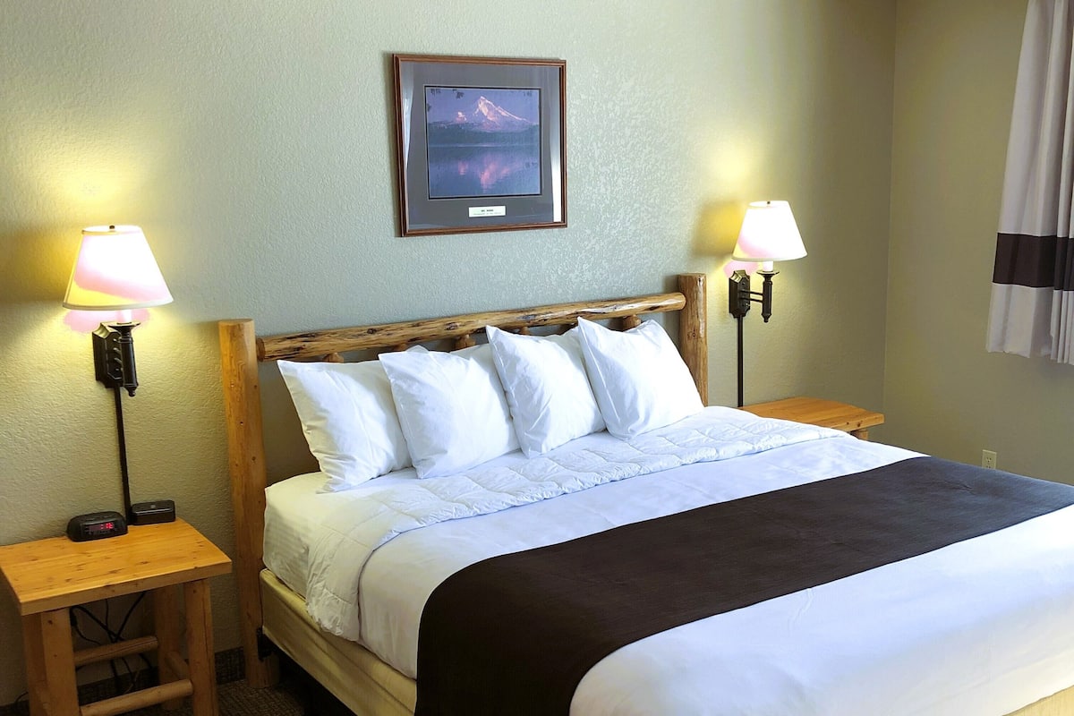 A neatly made bed with white and black bedding, two bedside tables with lamps, a framed picture on the wall, and a carpeted floor.