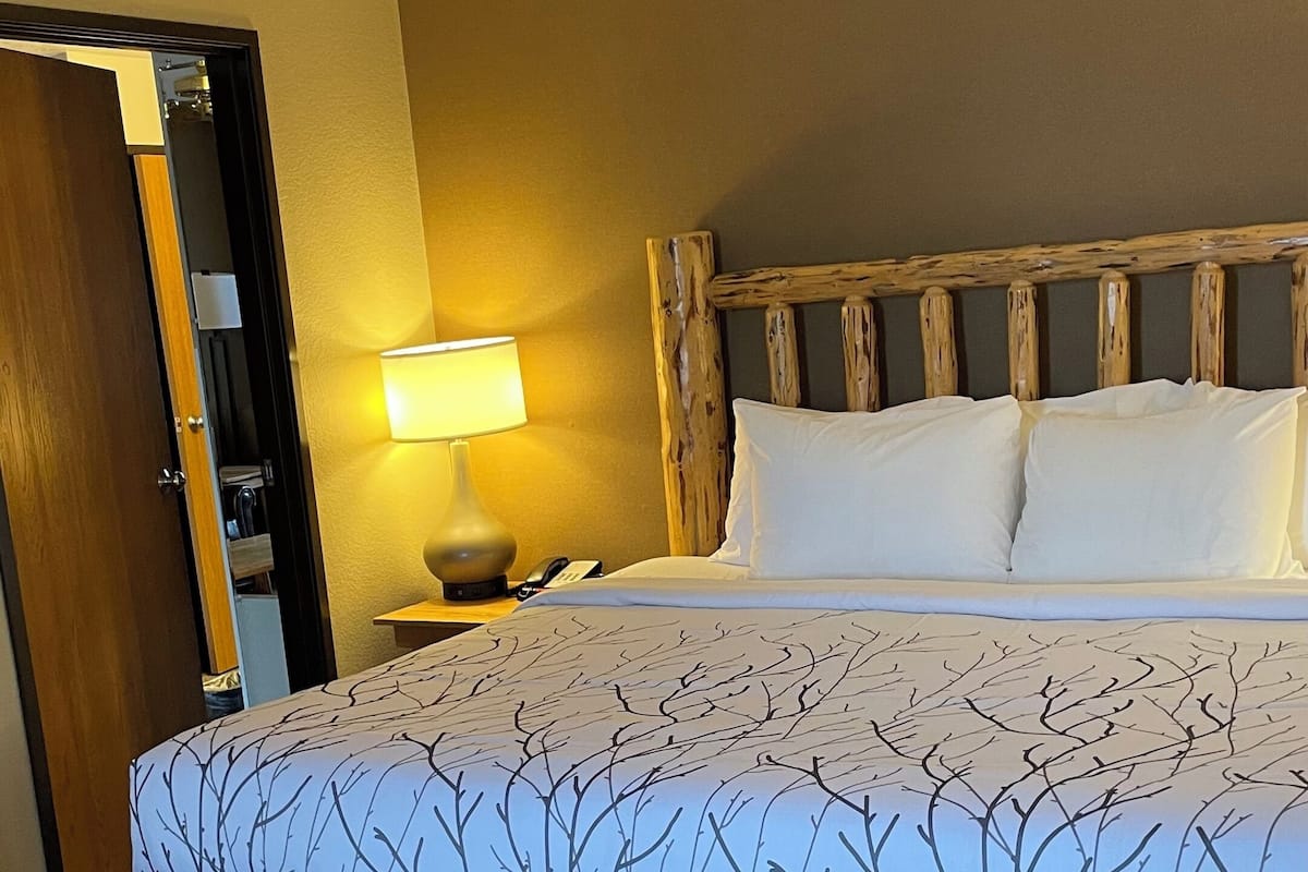 A hotel room with a bed, a ceiling fan, a nightstand with a lamp, and a wooden headboard.