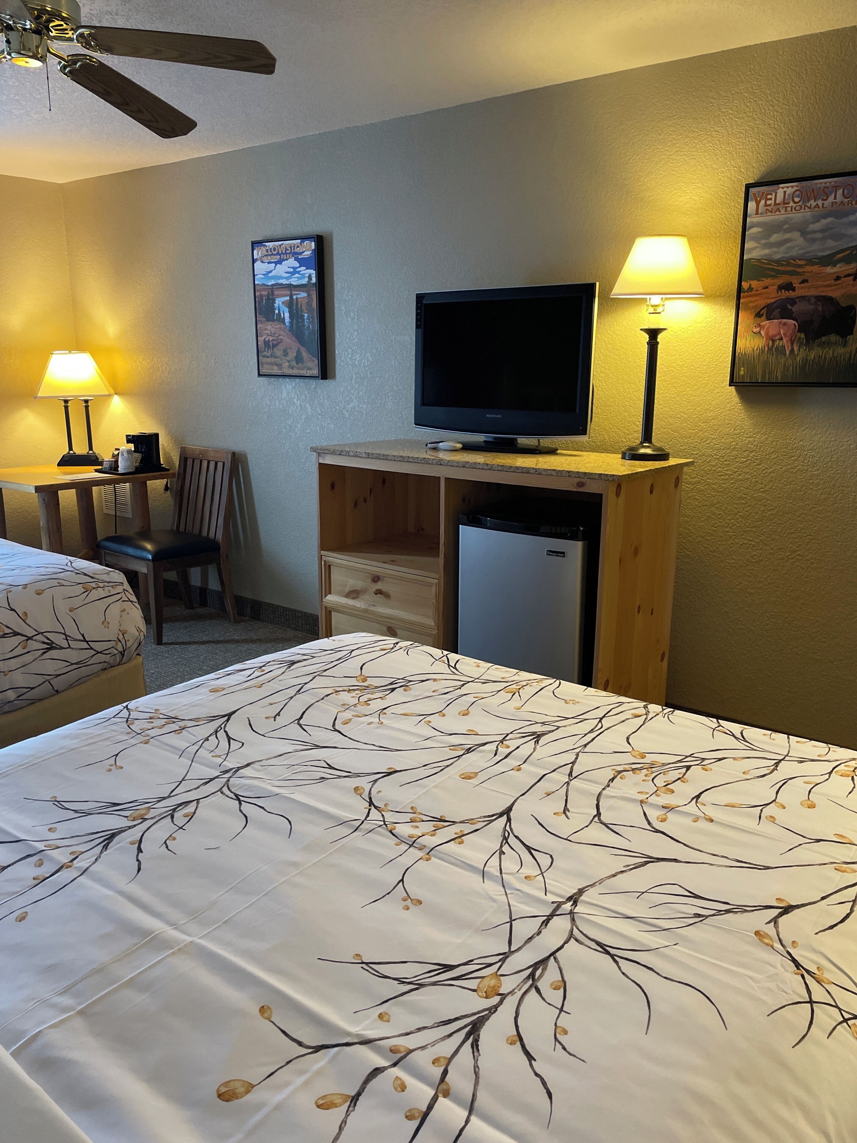 A hotel room with a bed, a desk with a television, a chair, a lamp, and a refrigerator.