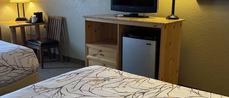 A hotel room with a bed, a desk with a television, a chair, a lamp, and a refrigerator.