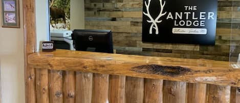 A reception desk with a wooden design, a sign for 'The Antler Lodge' in Yellowstone - Gardiner Mt., and a 'No Pets Allowed' sign.