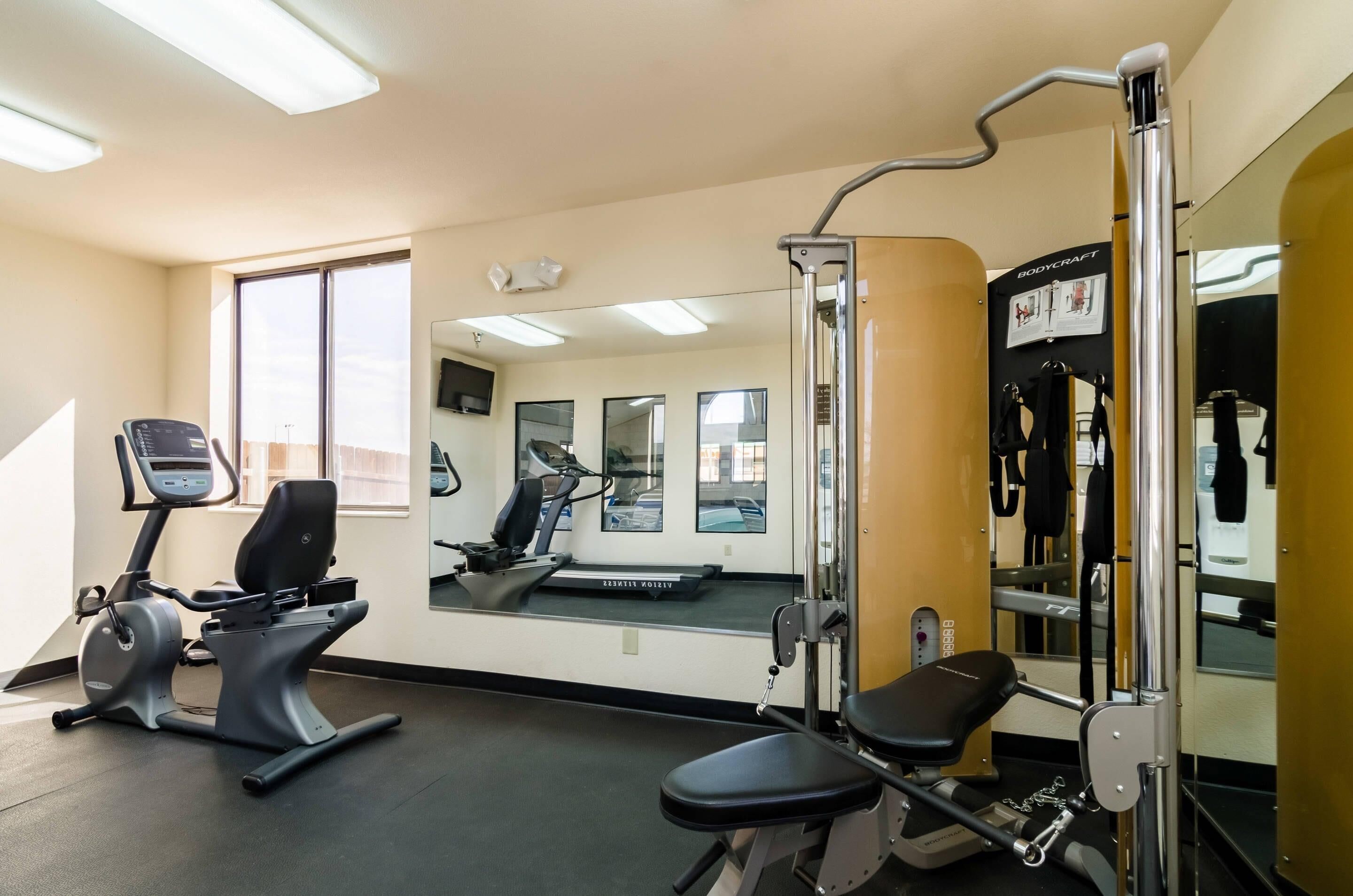 A gym with exercise equipment, a treadmill, and a mirror reflecting the room.
