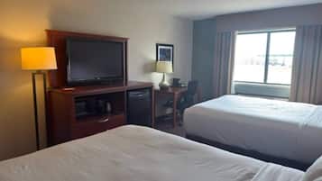 A hotel room with two beds, a desk with a television, a lamp, and a window with a view of the parking lot.