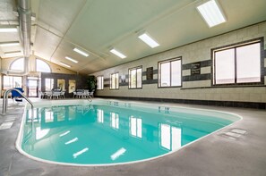An indoor swimming pool with clear water, a lifeguard on duty sign, and a sunlit ceiling.