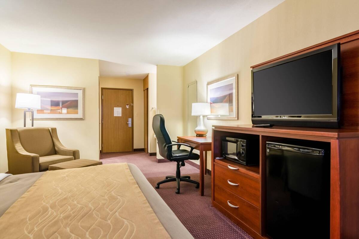 A hotel room with a bed, a desk, a television, a chair, and a microwave.