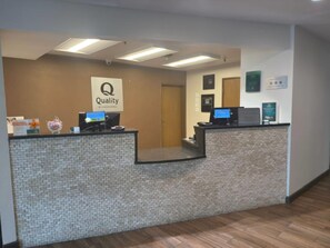 A reception desk with a 'Quality by Choice Hotels' sign, two computer monitors, and a brick-patterned counter. - Quality Inn & Suites Colby (Colby)