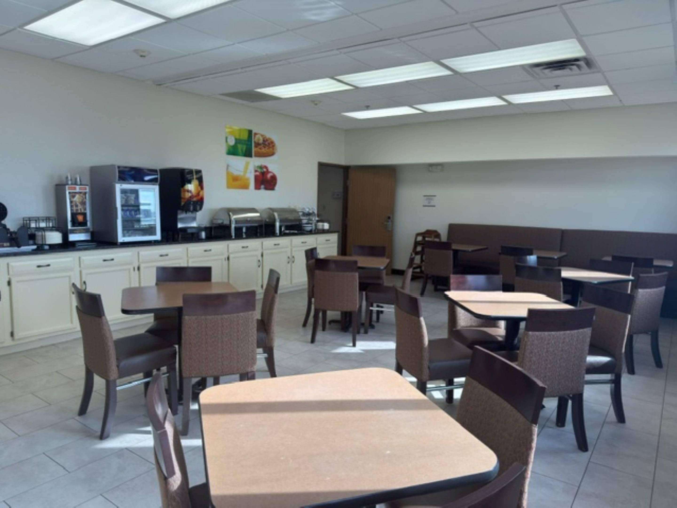 Eine Cafeteria mit Tischen, Stühlen, einem Kühlschrank und einer Buffet-Ecke.