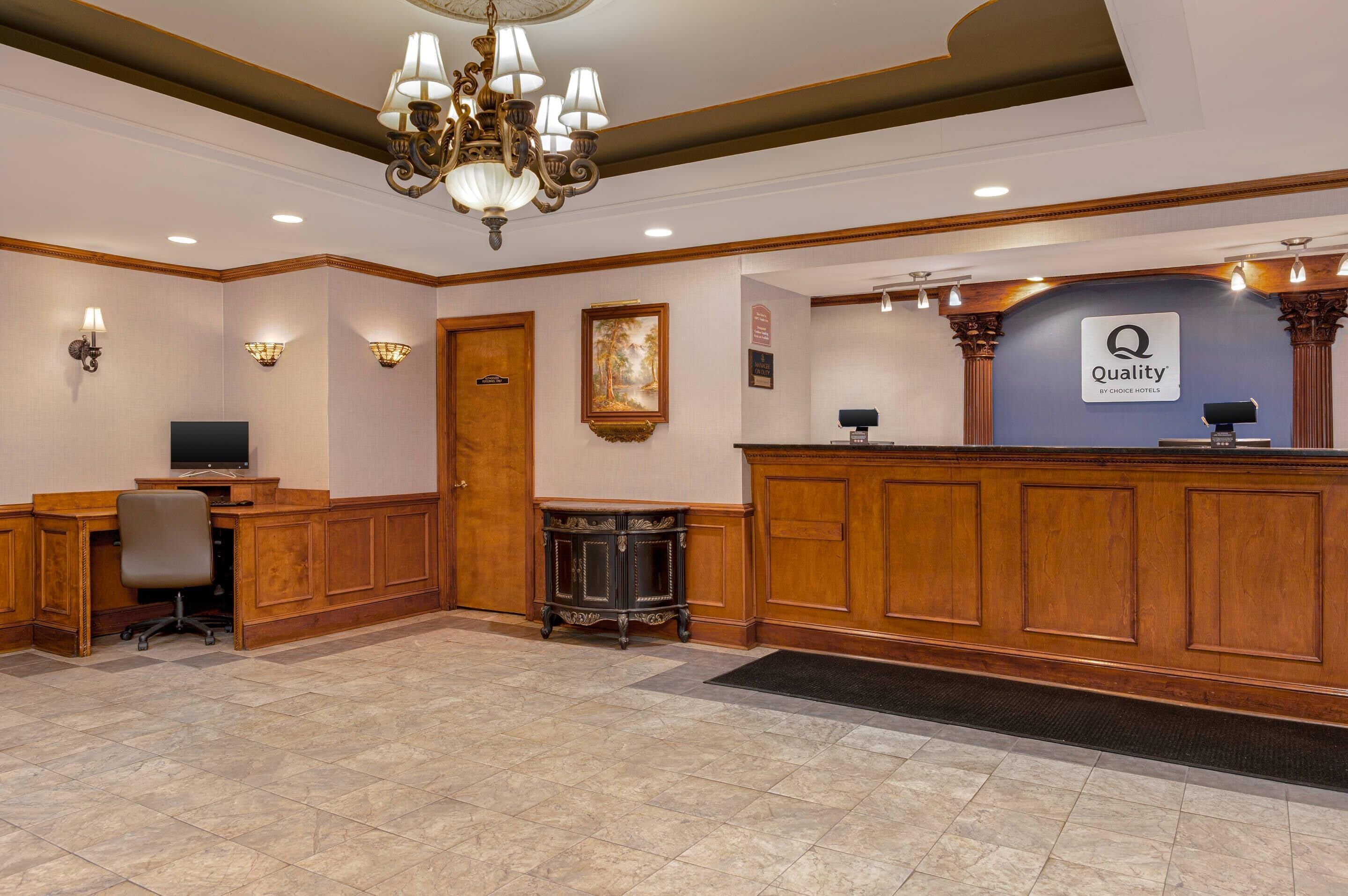A reception area with a wooden reception desk, a chandelier, a television, and a framed picture on the wall.
