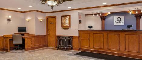 A reception area with a wooden reception desk, a chandelier, a television, and a framed picture on the wall.