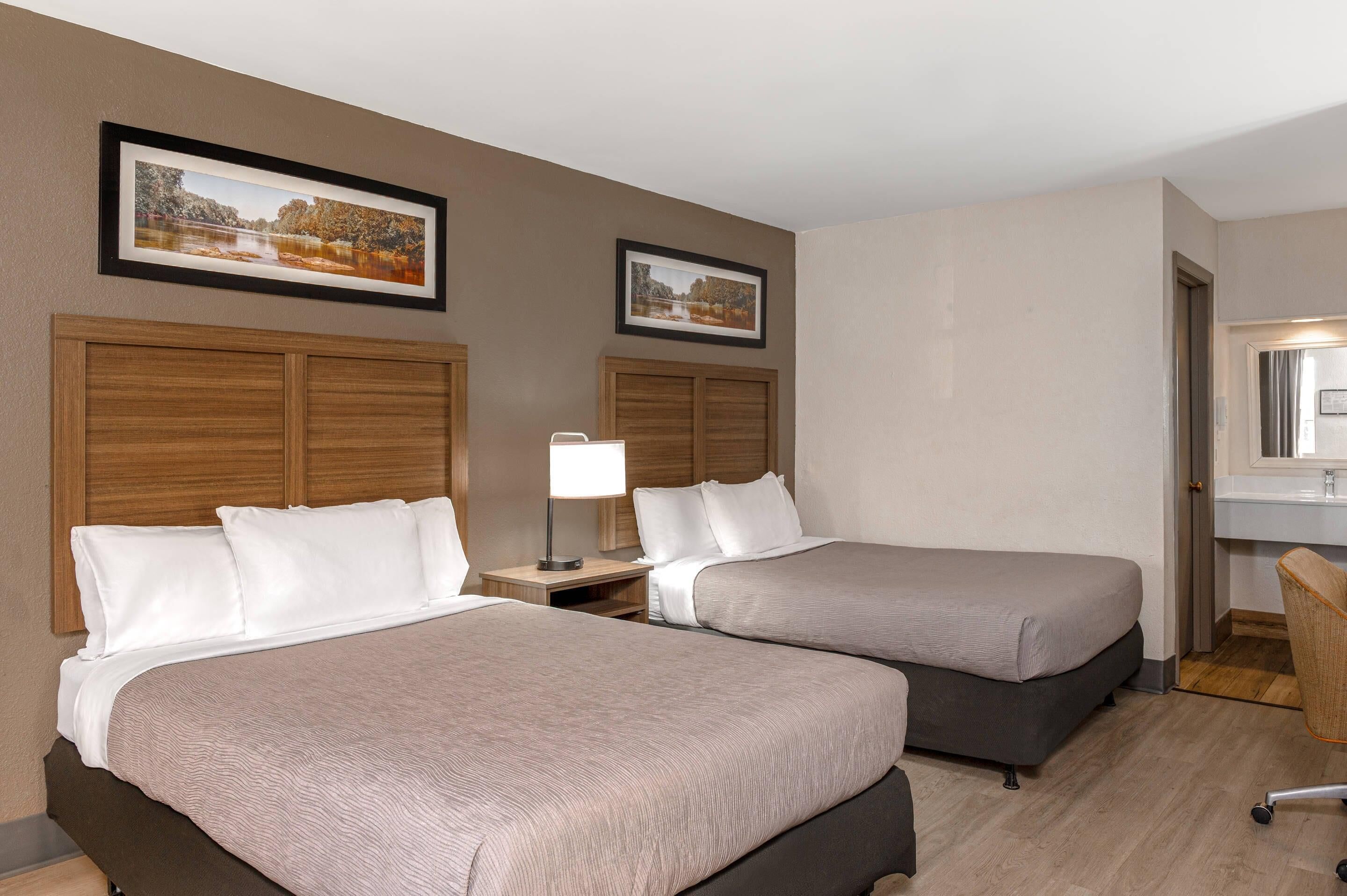 A hotel room with two beds, a nightstand with a lamp, a wooden headboard, and a framed picture on the wall.