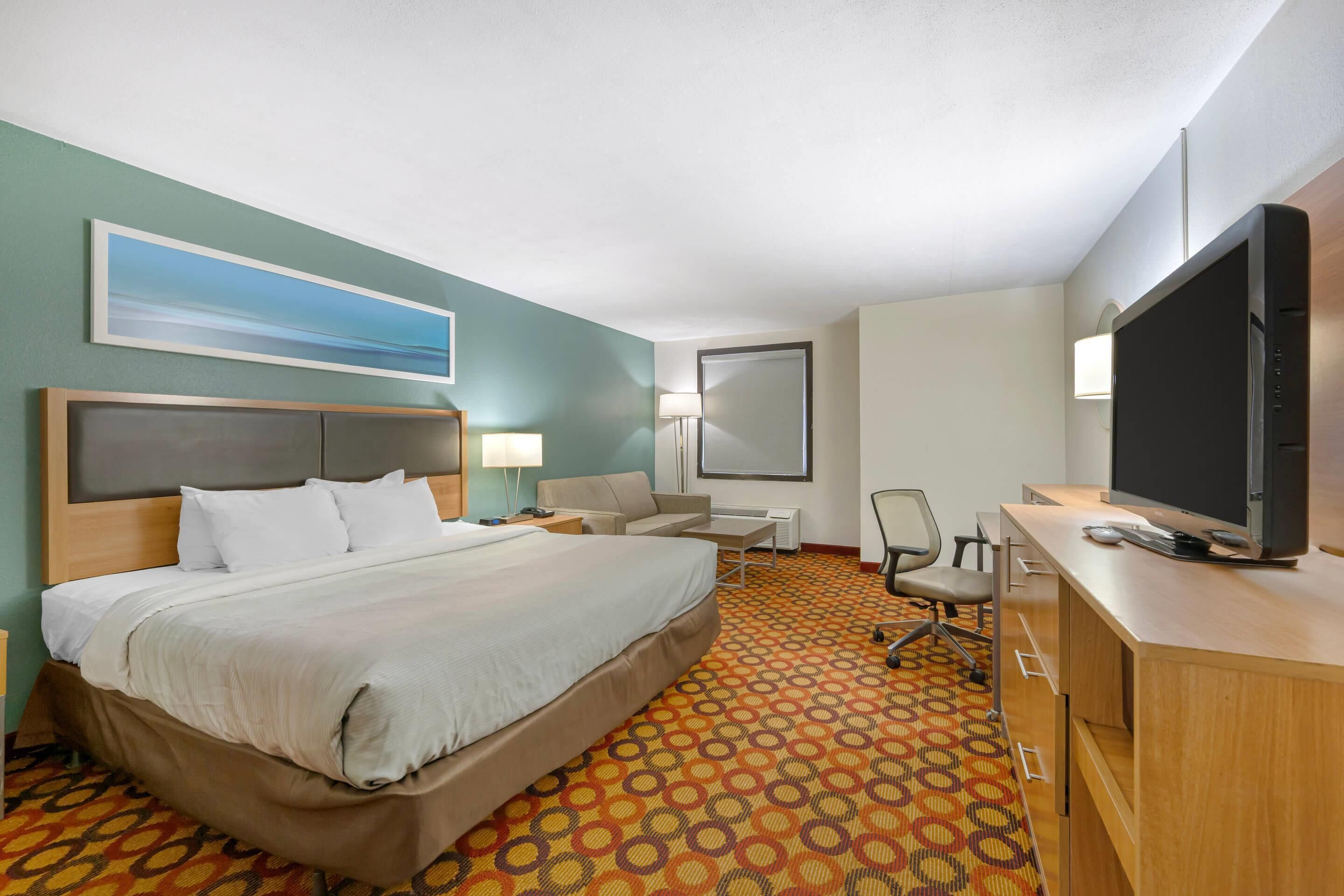 Ein Hotelzimmer mit Bett, Schreibtisch, Stuhl, Fernseher und einem Bild an der Wand.