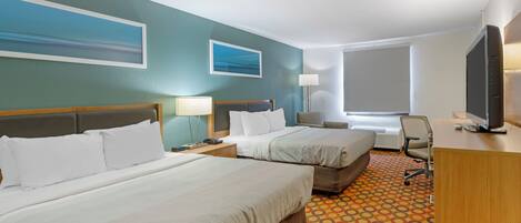 Quarto de hotel com duas camas, uma escrivaninha, televisão, luminária e janela com vista.