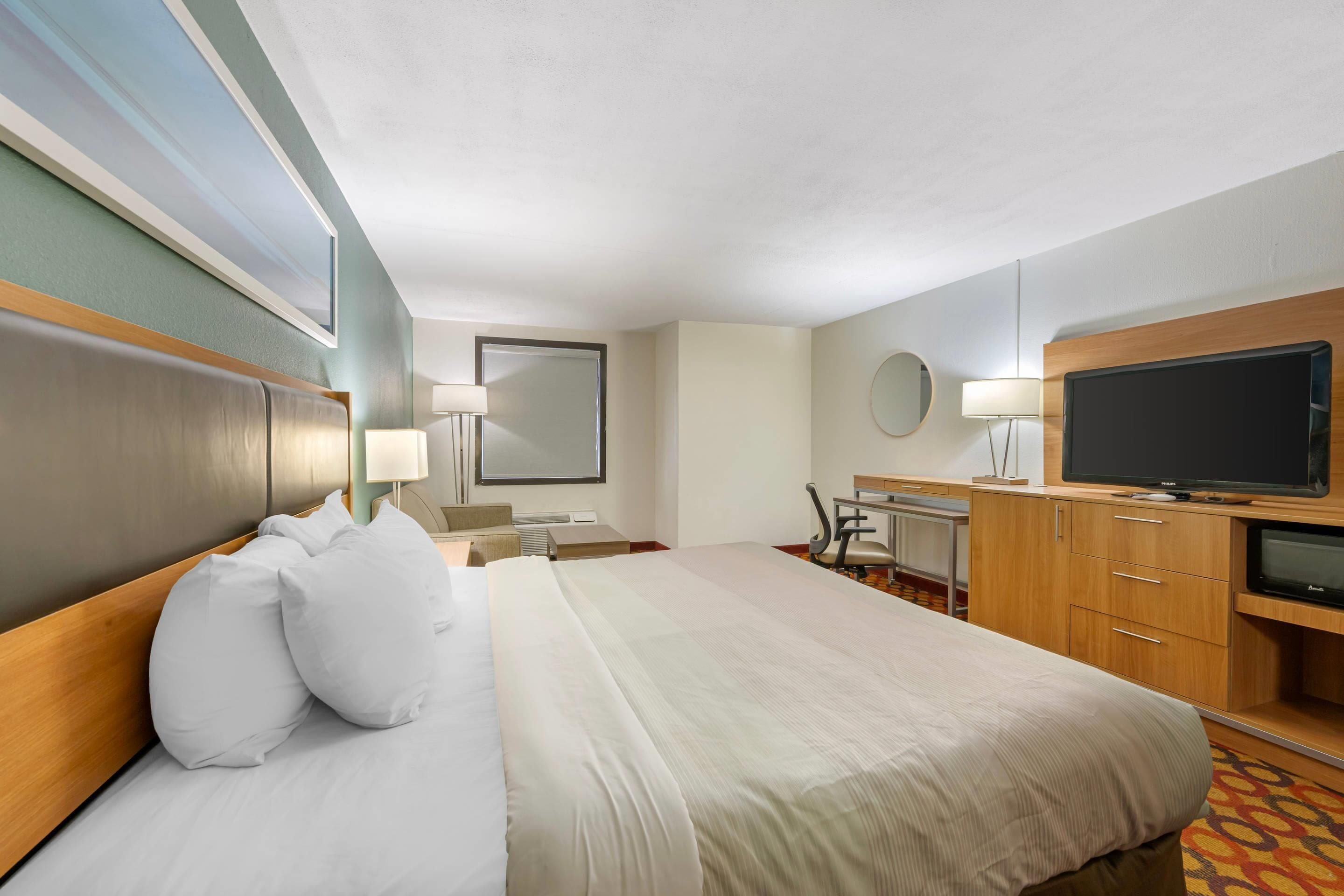 A hotel room with a large bed, a desk with a chair, a television, and a mirror.
