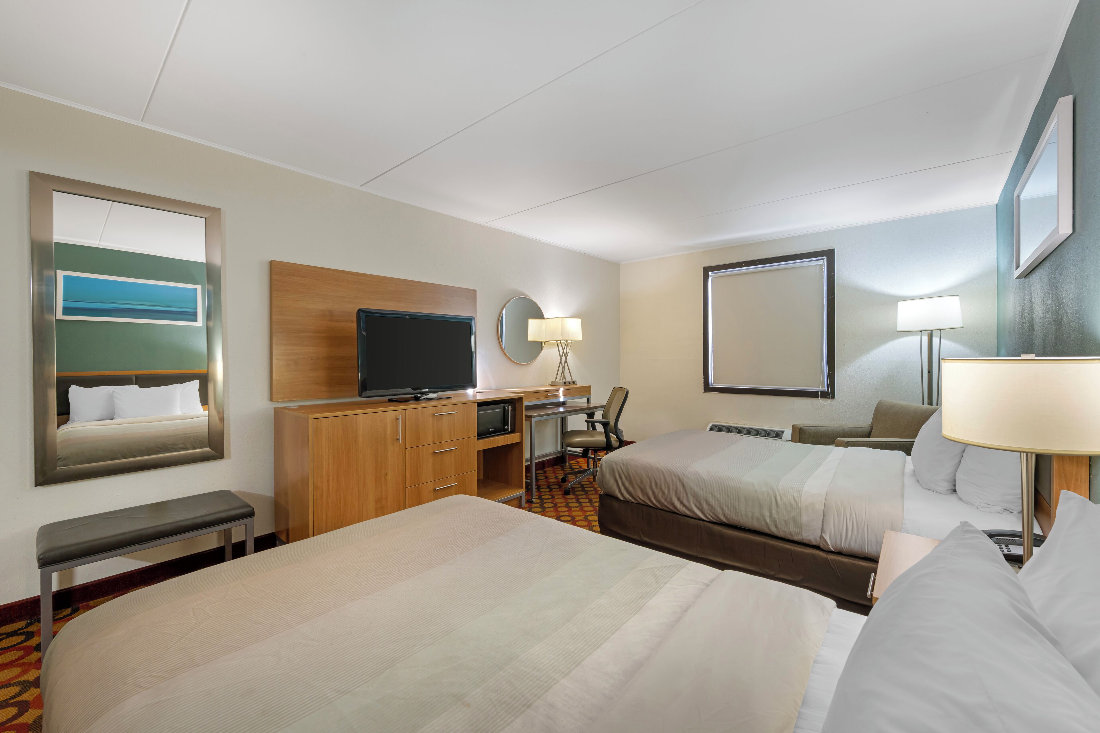 A hotel room with two beds, a desk with a computer, a television, and a mirror.