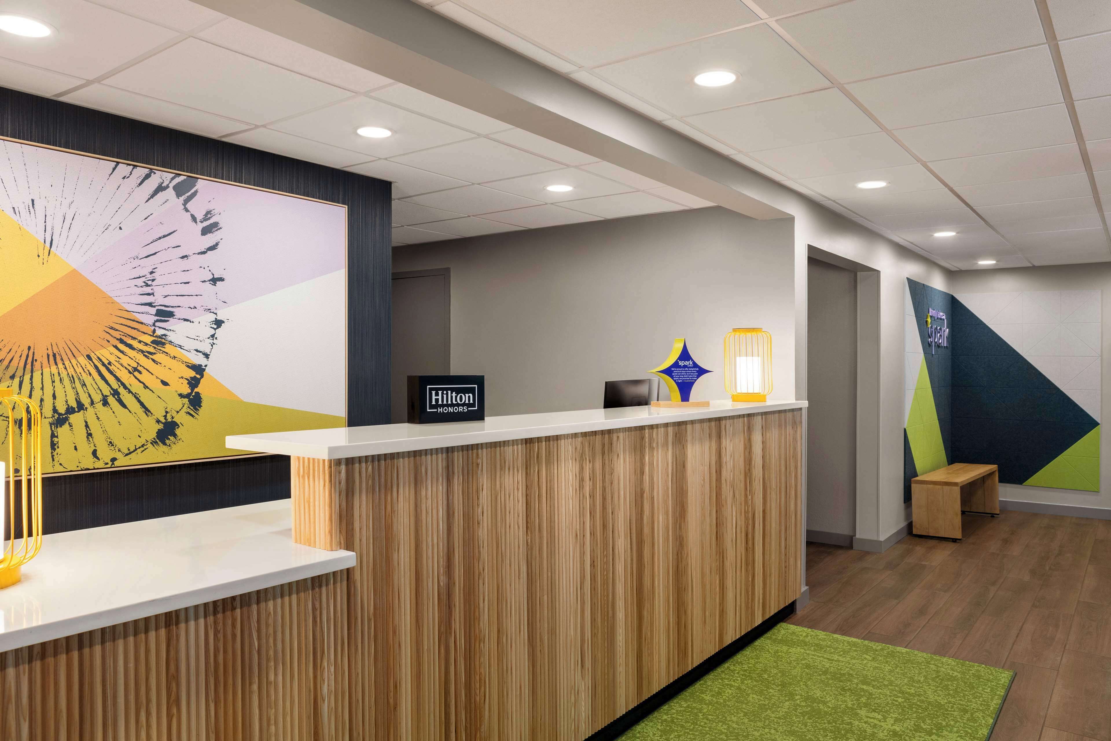 Un espace d’accueil moderne, avec un comptoir en bois, une grande peinture abstraite et un panneau indiquant « Hilton Honors ».