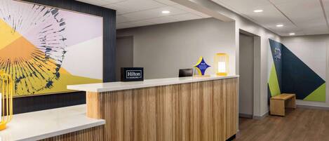 A modern hotel reception area with a wooden reception desk, a large abstract painting, and a "Hilton Honors" sign.