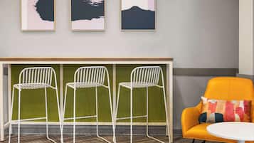 Une pièce moderne avec un séparateur de couleur verte, trois chaises en métal blanc, un fauteuil jaune et une table blanche.