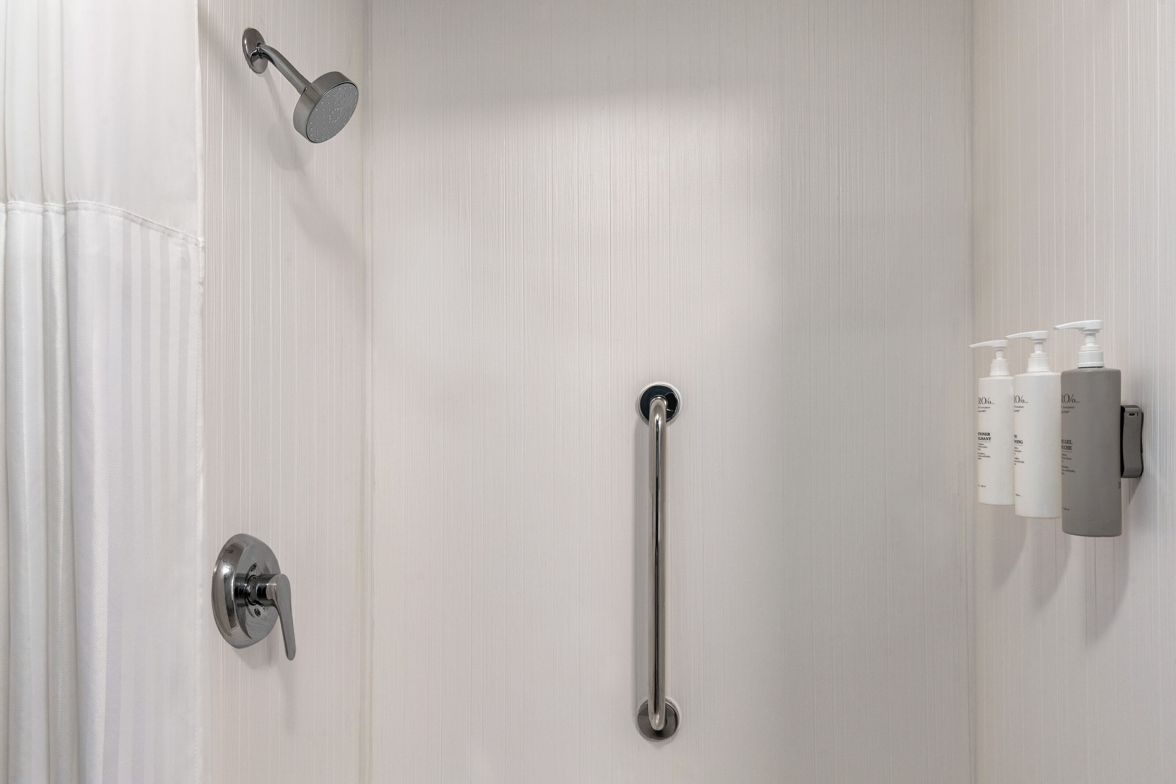 A bathroom with a shower, a grab bar, and toiletries on the wall.