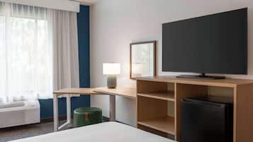 A hotel room with a bed, a desk with a lamp, a television, and a refrigerator.