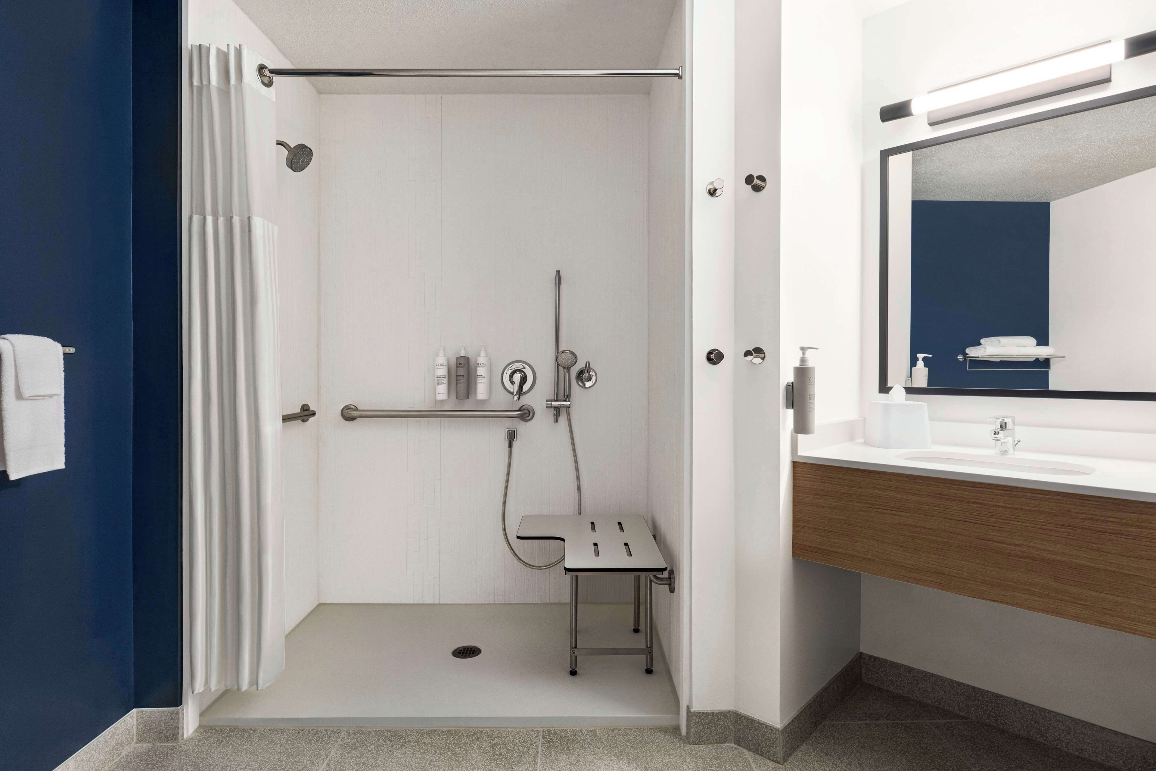 Un baño moderno con ducha, barra de apoyo y tocador con espejo.