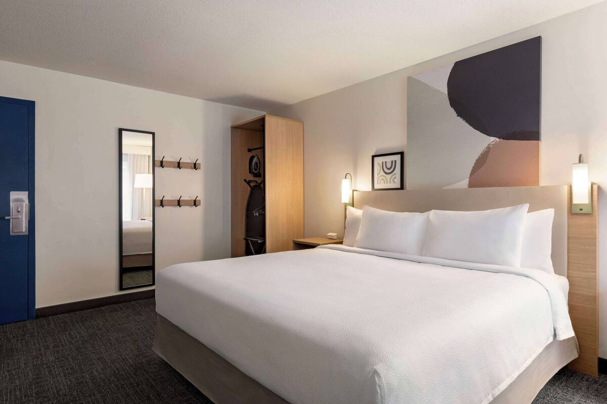 A hotel room with a large bed, a mirror, a coat rack, and a wardrobe.