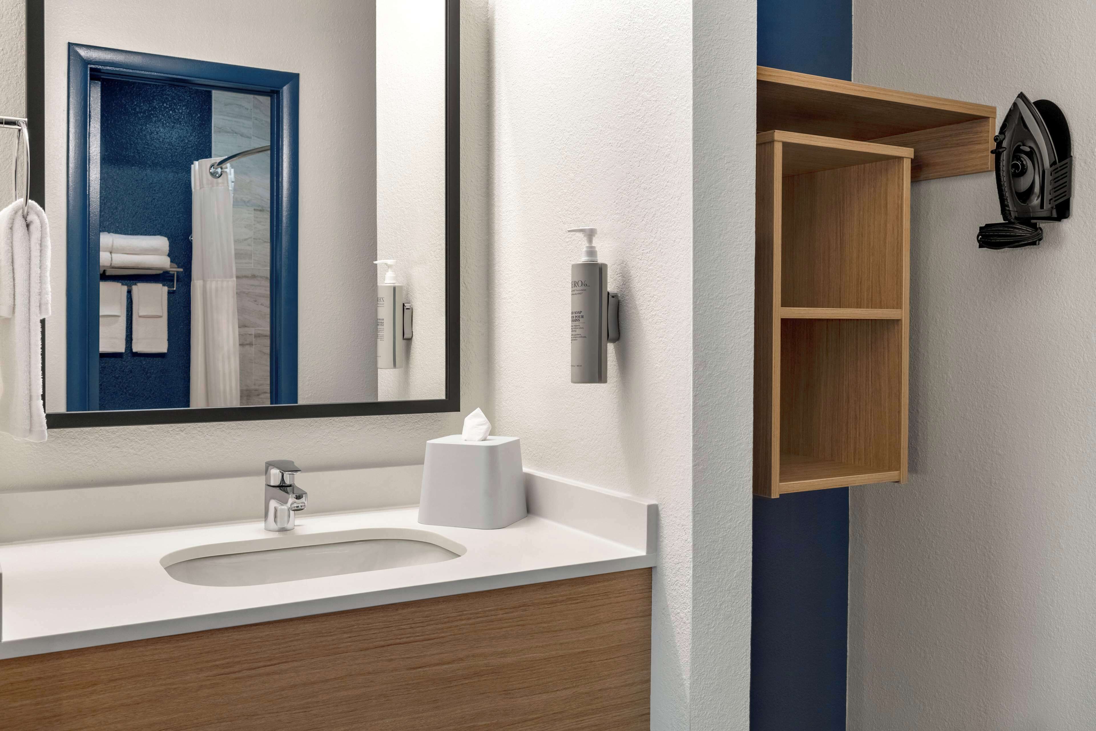 A modern bathroom with a large mirror, a sink, and a wooden cabinet with a hairdryer.