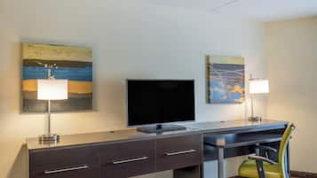 Une chambre d’hôtel équipée d’un bureau, de deux lampes, d’une télévision et de deux tableaux accrochés au mur.