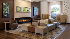A modern living room with a fireplace, comfortable seating, and artwork on the walls. - Holiday Inn Greensboro Coliseum by IHG (Greensboro)