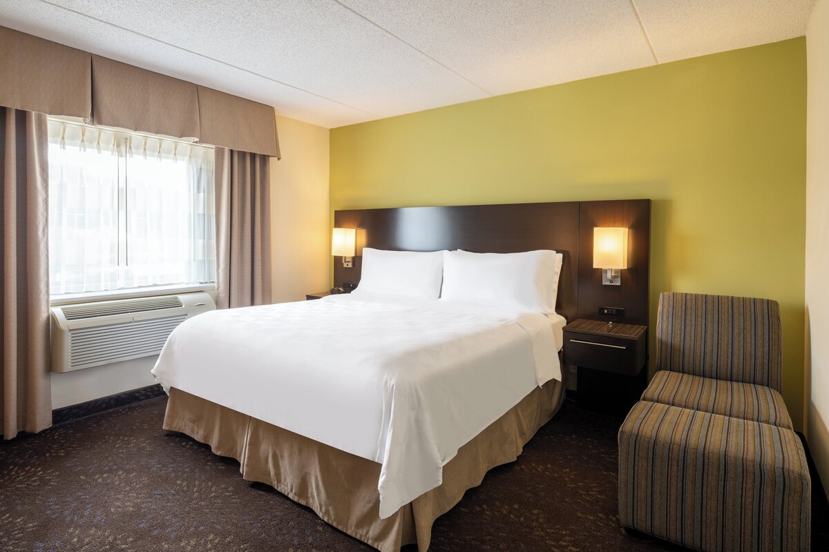 A hotel room with a large bed, two bedside lamps, a chair, and a window with curtains.