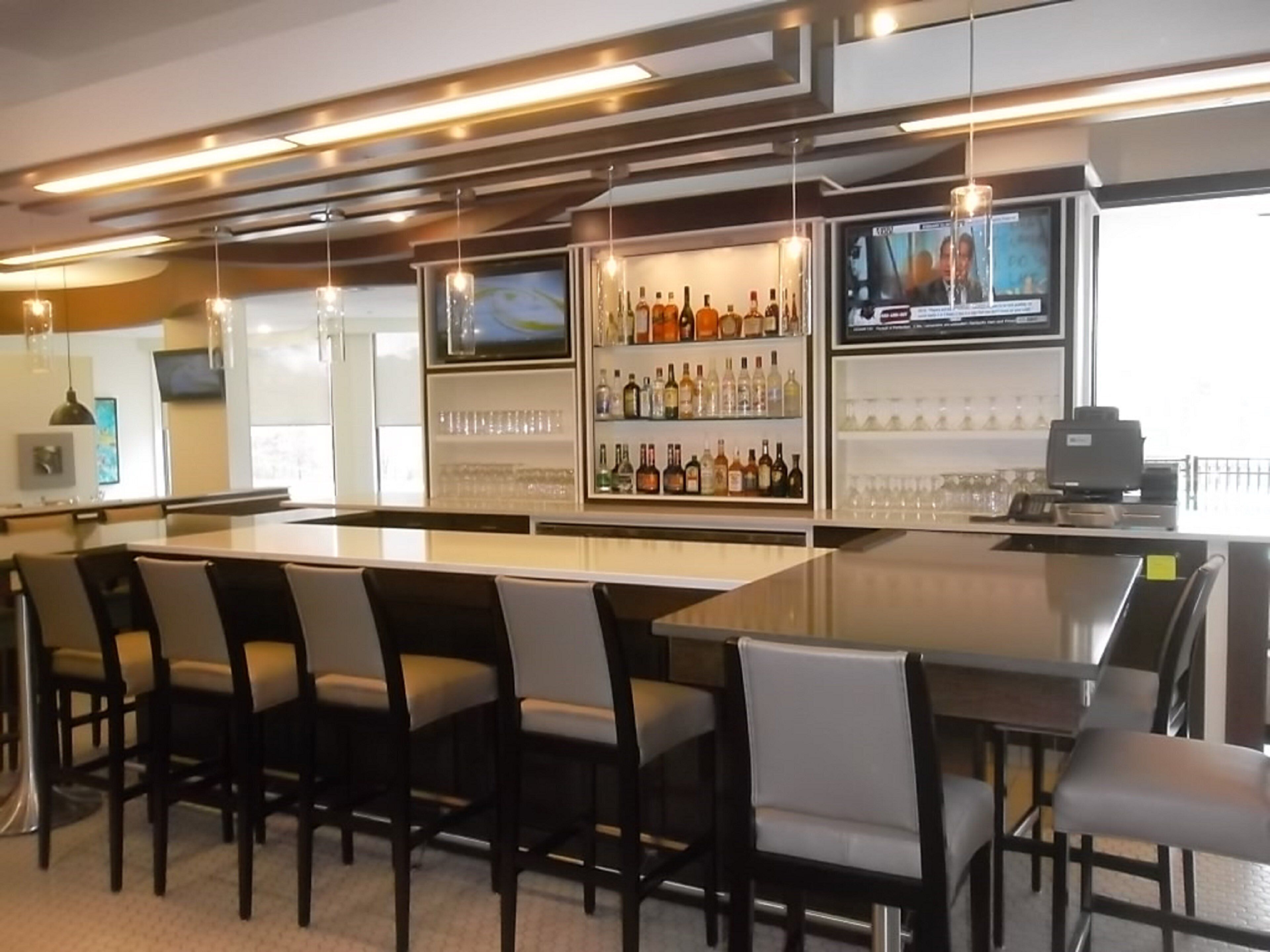 A bar area with a long counter, multiple seating options, and a television screen.