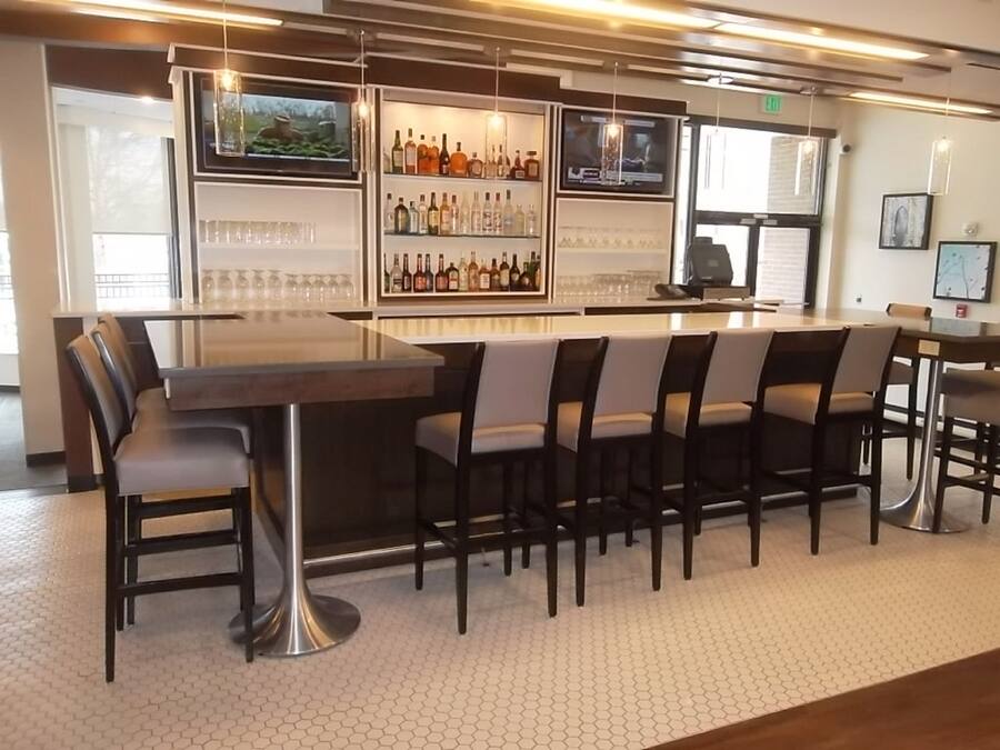 Zona de bar con una barra alargada, distintas opciones de asientos y una pantalla de televisión.