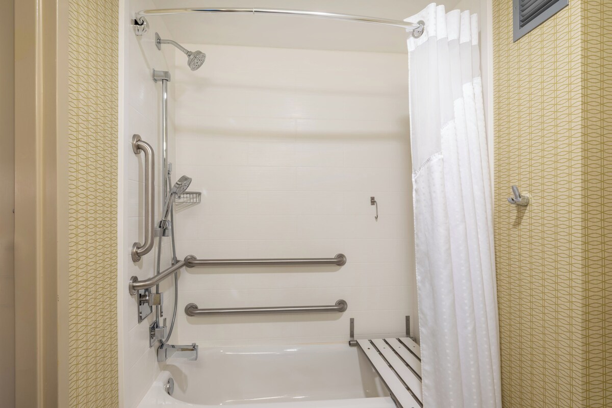 A walk-in shower with a bathtub, grab bars, and a showerhead.