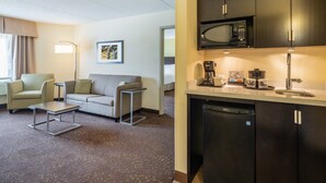 A compact hotel room with a kitchenette, a sofa, a small table, and a lamp. - Holiday Inn Greensboro Coliseum by IHG (Greensboro)