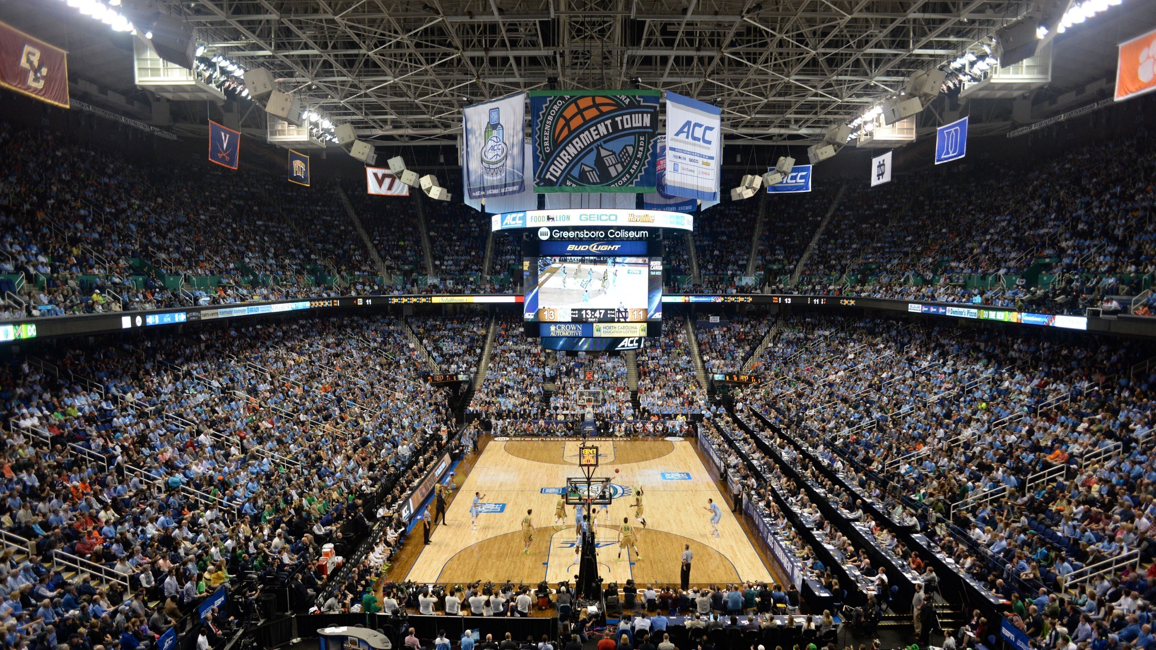 A basketball court with a scoreboard, surrounded by a large audience in a stadium.