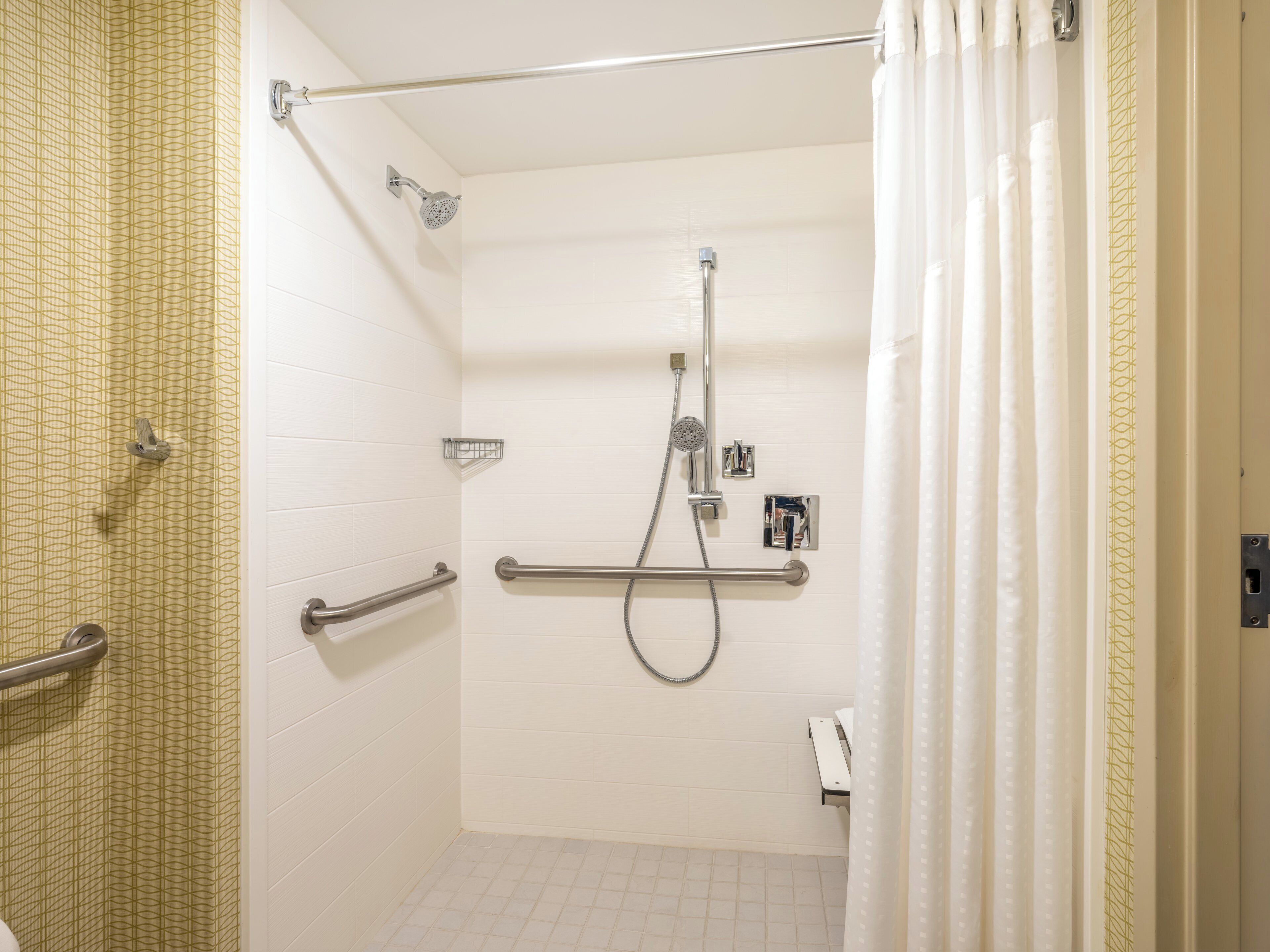 A bathroom with a shower, grab bars, and a towel rack.