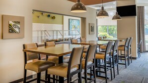A dining area with multiple tables and chairs, a kitchen area with a buffet, and artwork on the walls. - Holiday Inn Greensboro Coliseum by IHG (Greensboro)