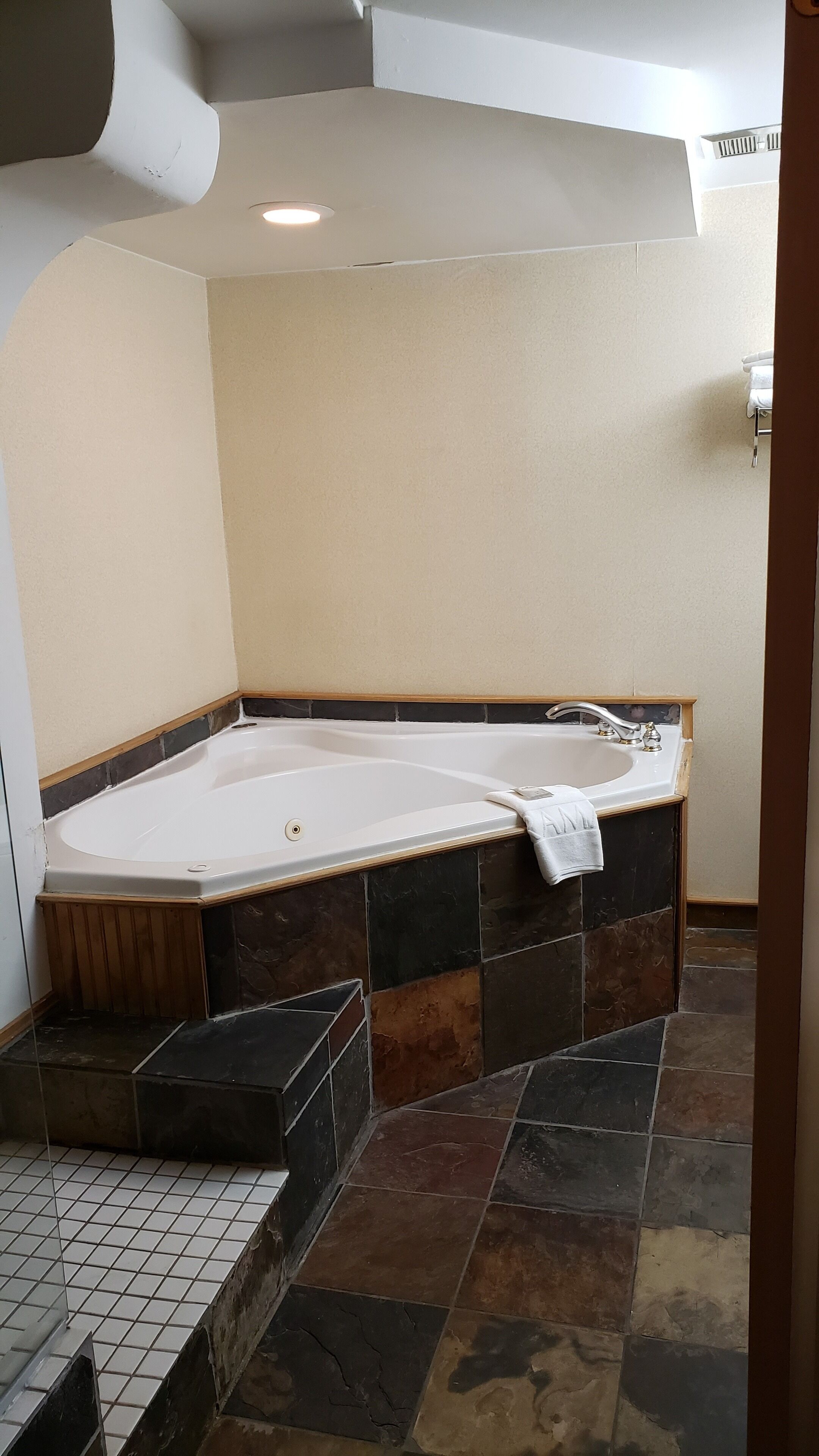 A bathroom with a large bathtub, tiled floor, and a shower area.