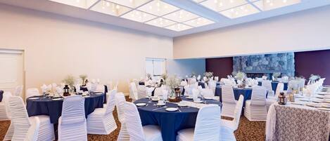 A conference room with round tables, white chairs, and a patterned carpet.