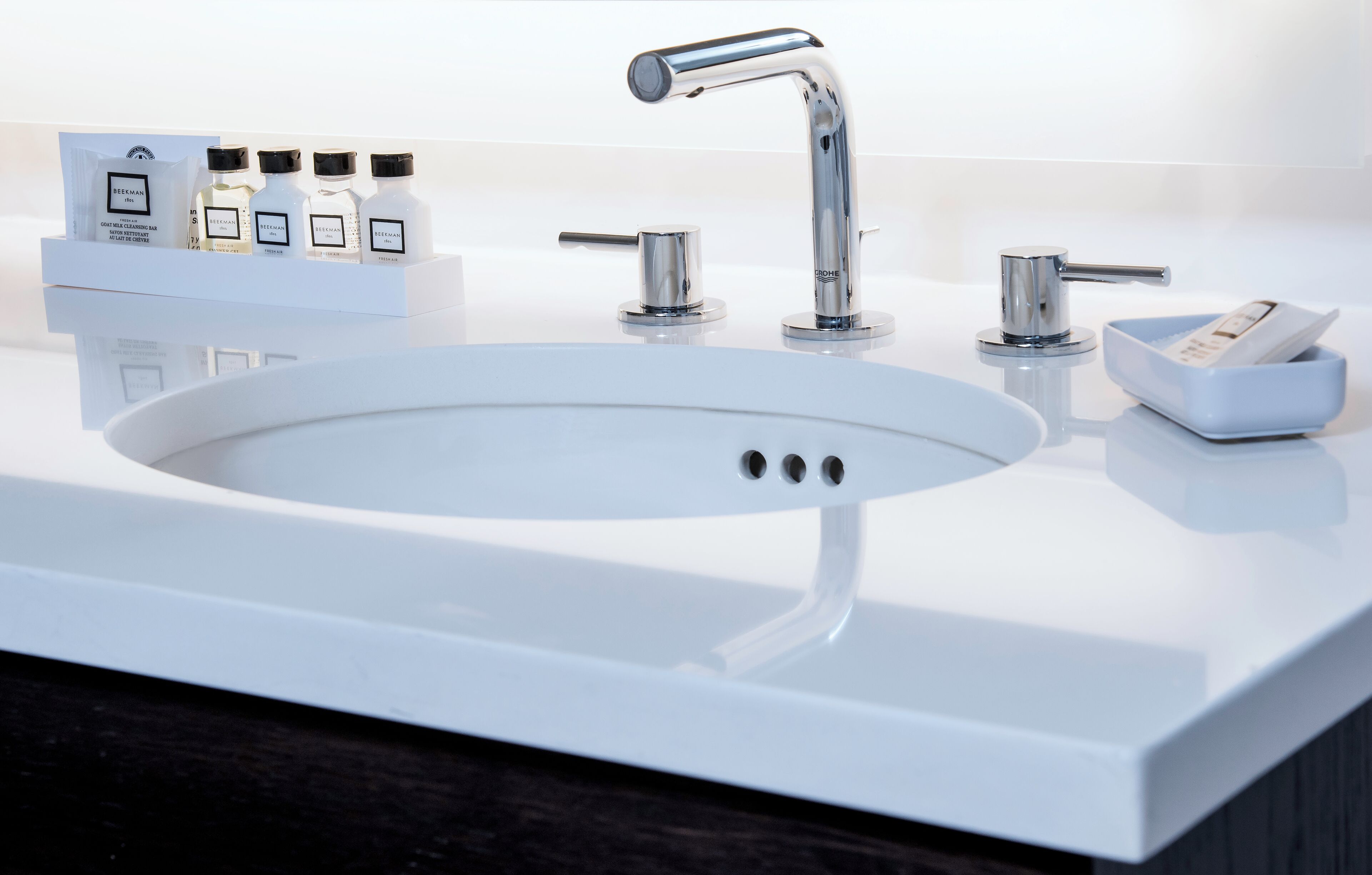 A modern bathroom sink with a chrome faucet, a soap dish, and a bottle of hand soap.